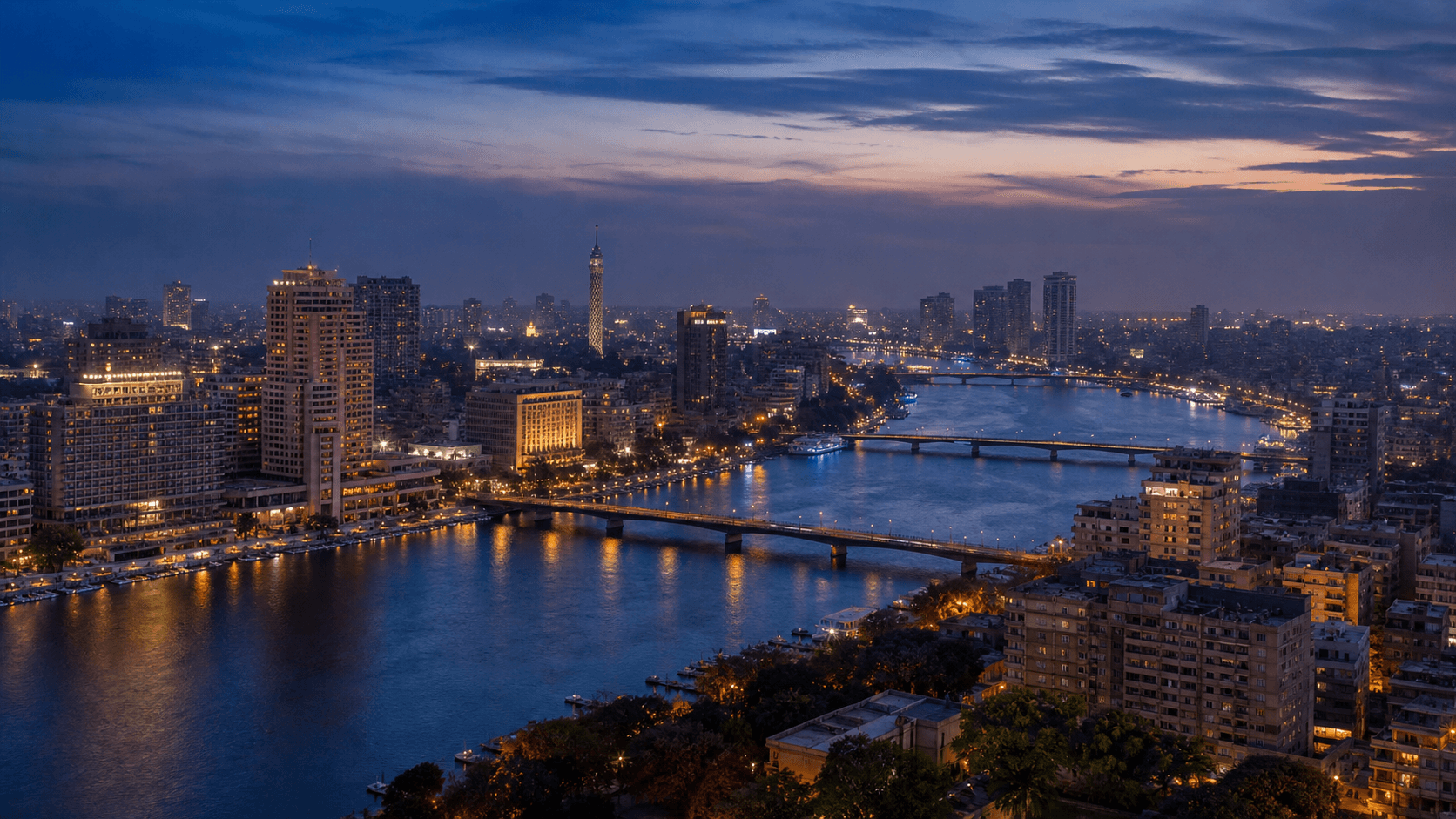 The Nile curves through the illuminated Cairo skyline at blue hour, with bridges and the Cairo Tower visible beneath a darkening sky.